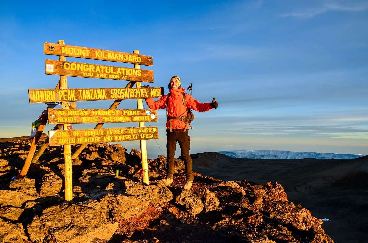 Kilimanjaro, Tanzania - March 11, 2015 A hiker standing on Uhuru Peak, the summit of Kibo and highest mountain in Africa, Mount Kilimanjaro at 5895m amsl. Summit sign and glacier in the background