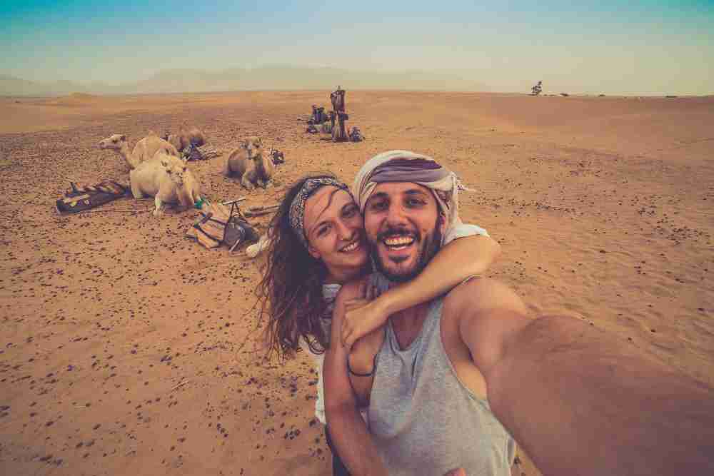 Young couple in love standing near many camels in africa desert taking photo with them, enjoying safari desert